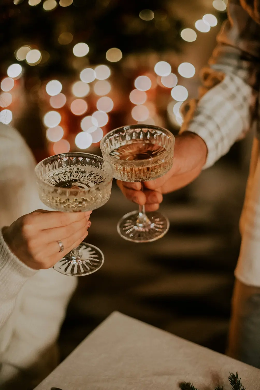 Deux personnes portent un toast avec des coupes de champagne en cristal, devant un arrière-plan festif aux lumières floues.