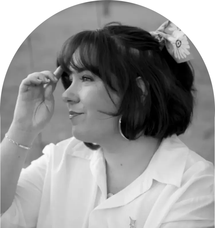 Portrait en noir et blanc de Lola G. créatrice de Petite Paillette, vue de profil, portant une chemise blanche et un accessoire de cheveux à motifs floraux.