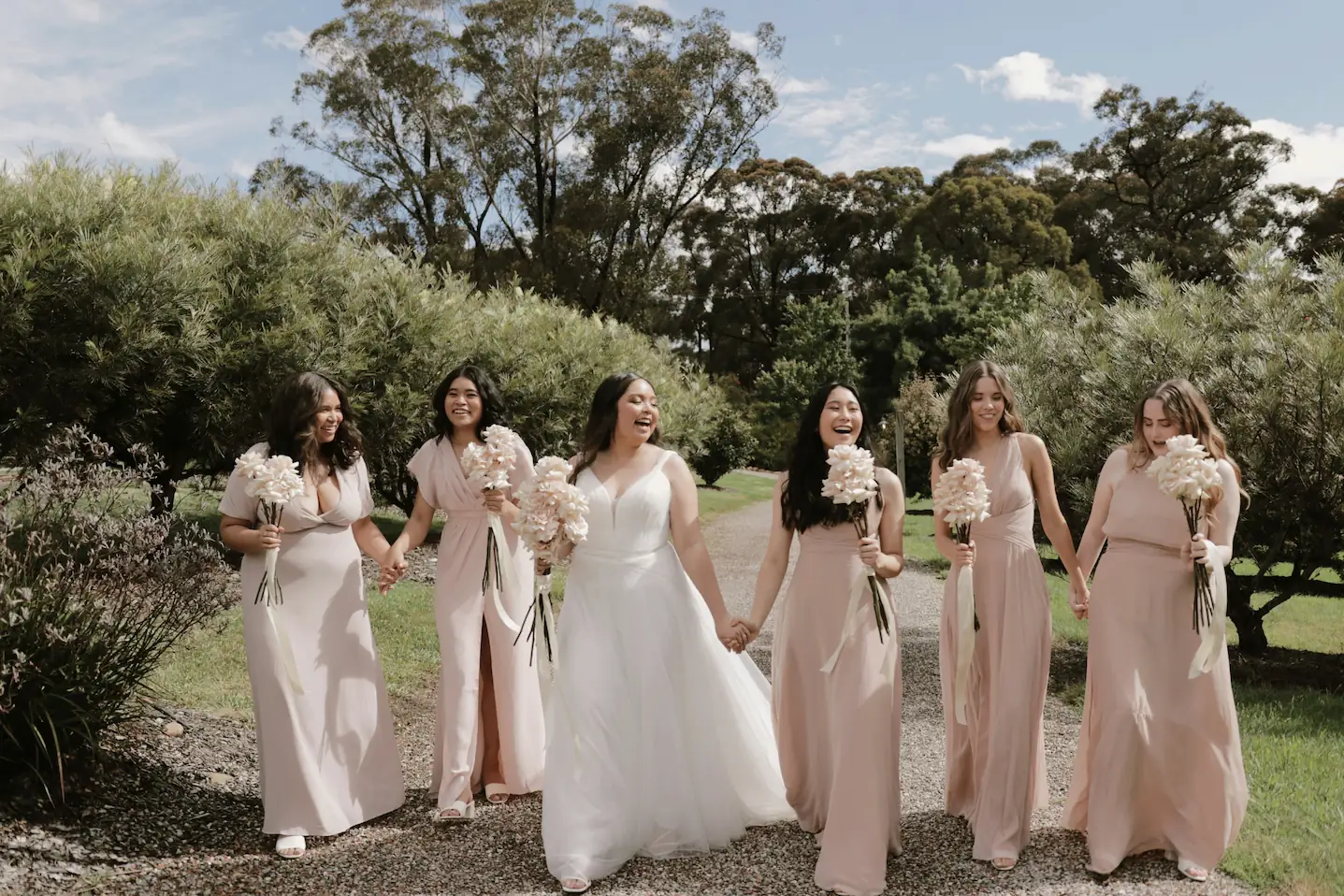 Mariée et demoiselles d'honneur marchant joyeusement dans un jardin.