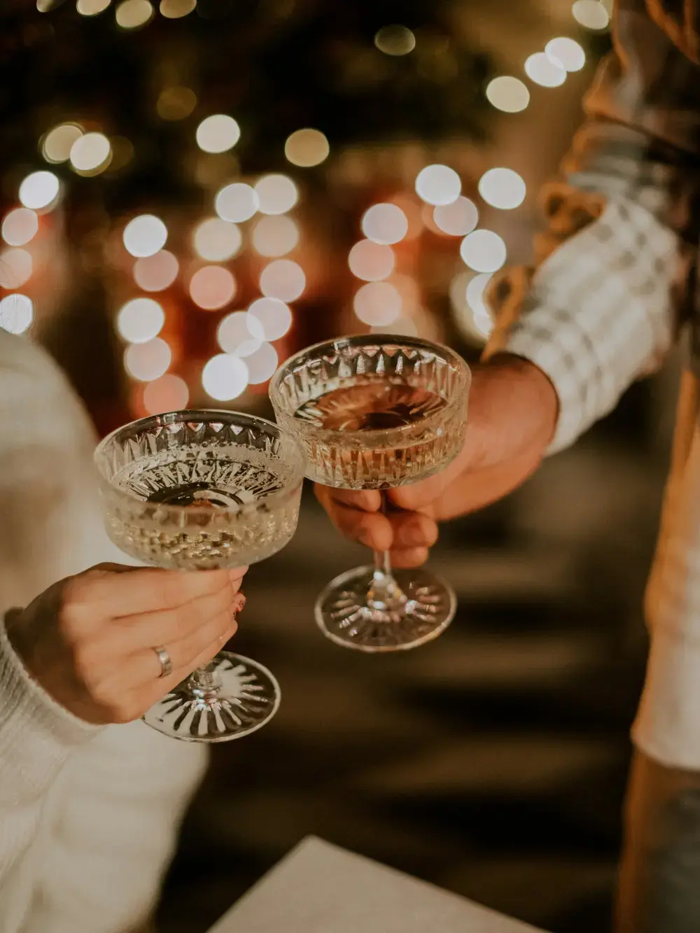 Deux personnes portent un toast avec des coupes de champagne en cristal devant des lumières de fête en arrière-plan.